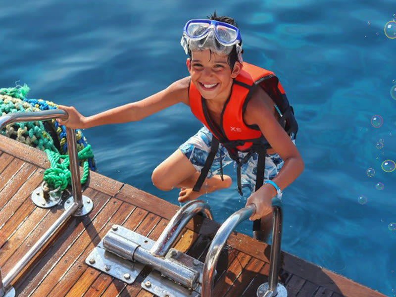 Child with dive mask and life jacket on the boat ladder